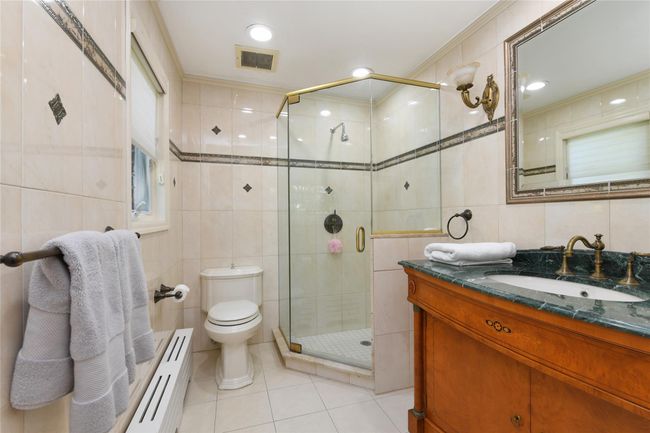 Bathroom with a baseboard radiator, tile walls, a shower stall, and tile patterned flooring | Image 13