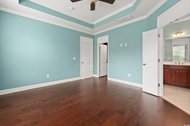 Unfurnished bedroom with a tray ceiling, visible vents, baseboards, ornamental molding, and dark wood finished floors | Image 19