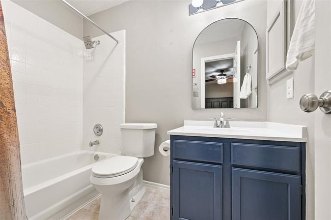 This updated bath services the previous bedroom with a modern navy vanity, arched mirror, and a tub/shower combo with classic white tile surround—both stylish and functional for guests or family. | Image 19