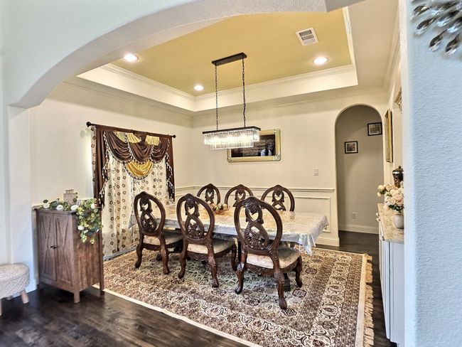 Dining space with arched walkways, a raised ceiling, crown molding, dark wood-style floors, and baseboards | Image 9
