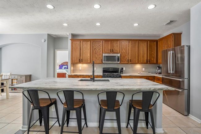 This chef-inspired kitchen features luxurious leathered granite counters, a massive island with an eating bar, and a deep single-basin undermount sink with a sleek pull-down faucet. Stainless steel appliances and tall upper cabinets offer both style and ample storage. | Image 10