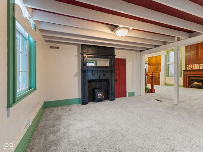 unfurnished living room with a wood stove, carpet, a lit fireplace, beamed ceiling, and visible vents | Image 6
