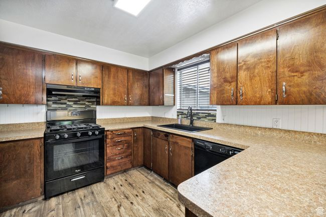 Kitchen featuring black appliances, a sink, light wood-style flooring, light countertops, and dark brown cabinets | Image 12