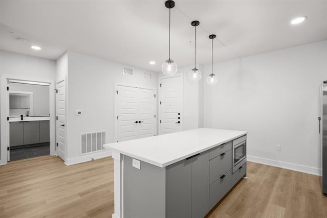 Kitchen featuring gray cabinets, stainless steel microwave, light wood-type flooring, recessed lighting, and hanging light fixtures | Image 4