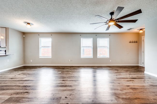Empty room with a textured ceiling, ceiling fan, wood finished floors, and baseboards | Image 6