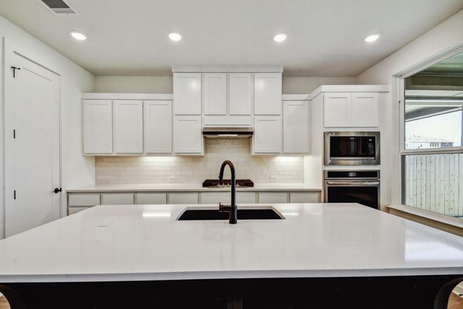 Kitchen featuring stainless steel appliances, decorative backsplash, light countertops, custom exhaust hood, and recessed lighting | Image 7