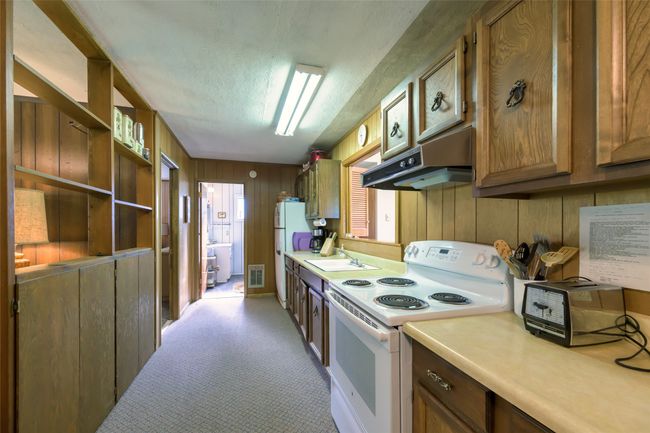 Kitchen with white appliances, under cabinet range hood, light countertops, a textured ceiling, and light carpet | Image 26