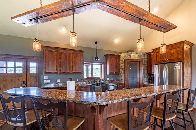 Kitchen with freestanding refrigerator, a kitchen bar, decorative light fixtures, and dark stone countertops | Image 13