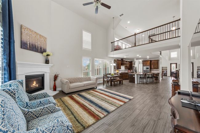 Living area featuring a towering ceiling, a ceiling fan, a glass covered fireplace, wood finished floors, and baseboards | Image 15