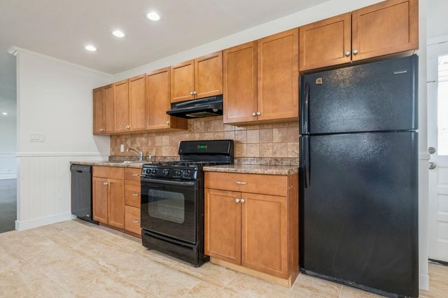 Kitchen featuring ornamental molding, black appliances, under cabinet range hood, a sink, and backsplash | Image 13