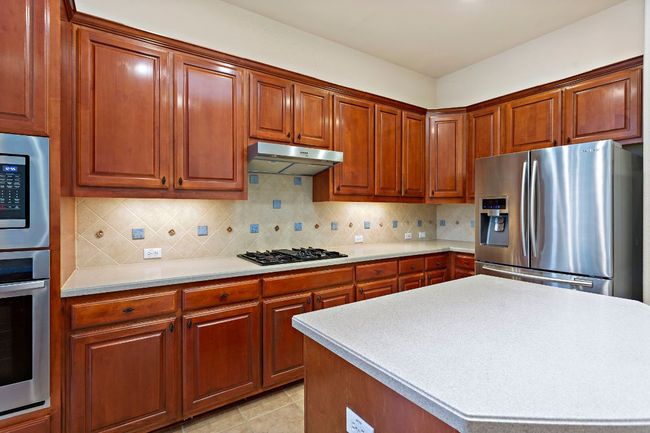 Kitchen featuring under cabinet range hood, appliances with stainless steel finishes, tasteful backsplash, and light countertops | Image 12