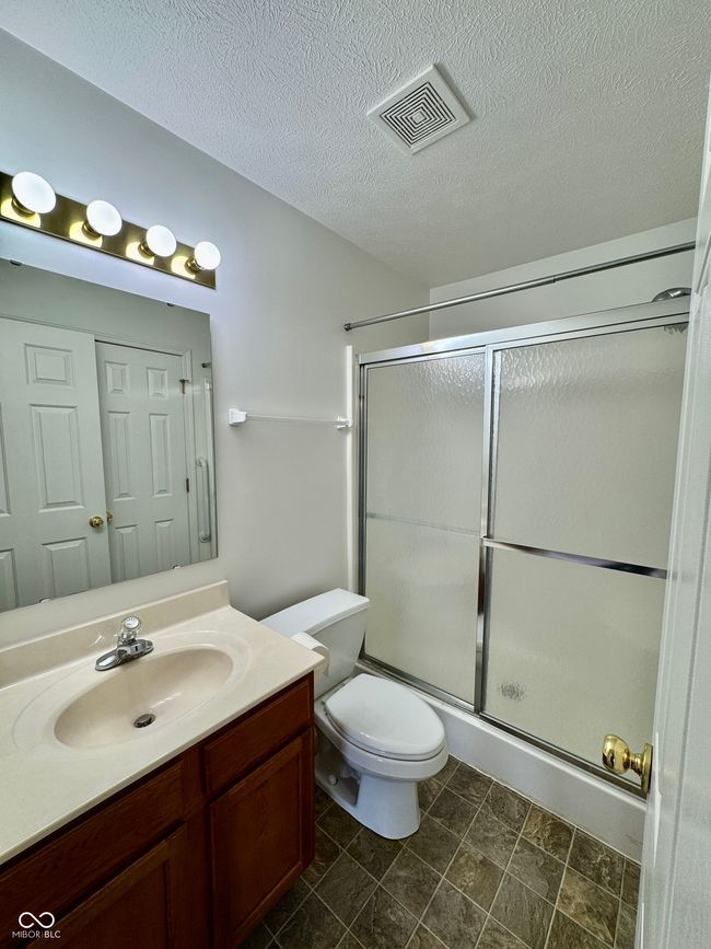 bathroom with a shower with shower door, visible vents, toilet, a textured ceiling, and vanity | Image 13
