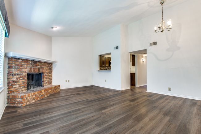 Unfurnished living room with high vaulted ceiling, dark hardwood / wood-style flooring, a brick fireplace, and a chandelier | Image 6