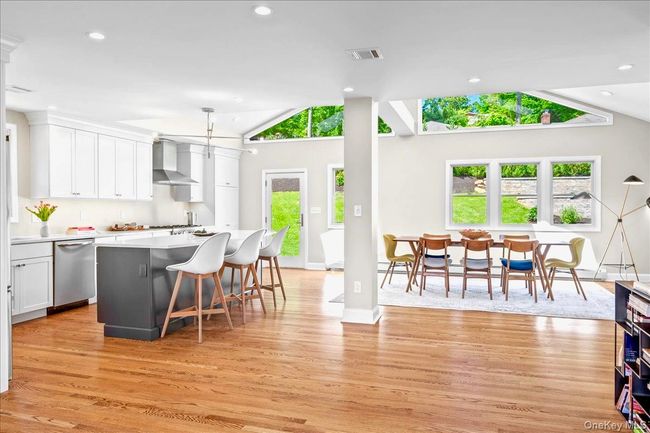 Kitchen featuring stainless steel dishwasher, wall chimney range hood, lofted ceiling, light wood flooring, and white cabinets | Image 7