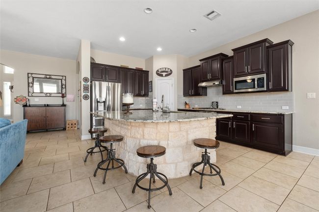 Kitchen with light stone countertops, a breakfast bar, appliances with stainless steel finishes, under cabinet range hood, and visible vents | Image 8