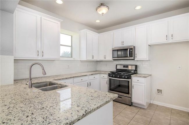 Kitchen featuring appliances with stainless steel finishes, white cabinets, backsplash, light stone counters, and recessed lighting | Image 12