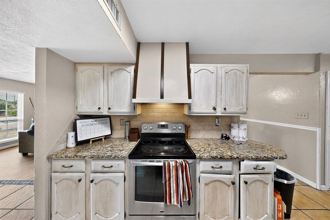 Kitchen featuring stainless steel range with electric cooktop, backsplash, wall chimney range hood, light tile patterned floors, and baseboards | Image 8