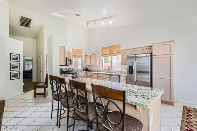 Kitchen with appliances with stainless steel finishes, high vaulted ceiling, light brown cabinets, light tile patterned flooring, and a kitchen breakfast bar | Image 10