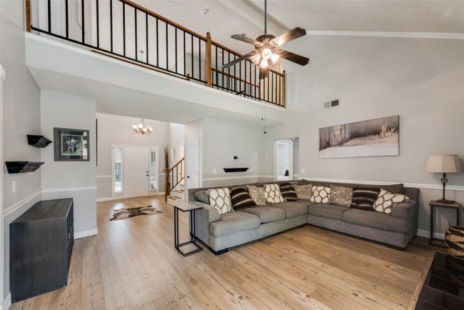 Living room with stairway, high vaulted ceiling, wood finished floors, a chandelier, and ceiling fan | Image 9
