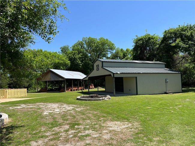 View of yard featuring an outdoor fire pit, a pole building, a detached carport | Image 6