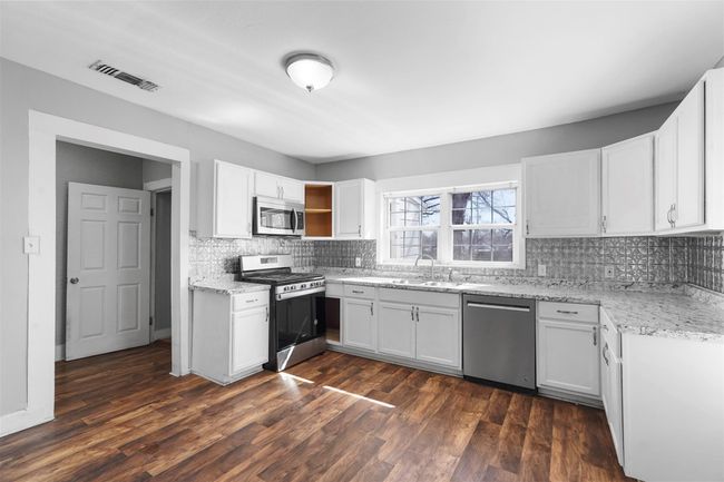 Kitchen featuring stainless steel appliances, tasteful backsplash, light stone counters, dark wood-style floors, and white cabinetry | Image 4