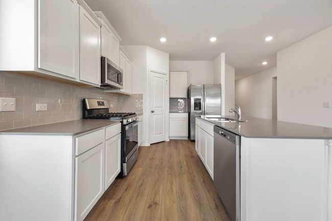 Kitchen with stainless steel appliances, light wood-style flooring, white cabinets, tasteful backsplash, and a center island with sink | Image 15