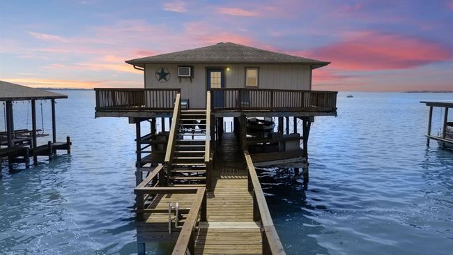 This photo features a charming overwater boathouse at sunset, connected by a wooden walkway, offering serene lake views and a unique waterfront living experience. | Image 29