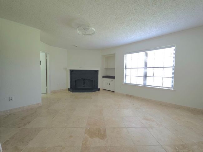 Unfurnished living room featuring a textured ceiling and a fireplace with raised hearth | Image 13