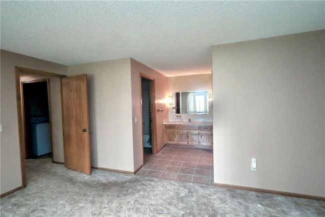Unfurnished bedroom featuring light colored carpet, ensuite bathroom, a textured ceiling, and washer / dryer | Image 34