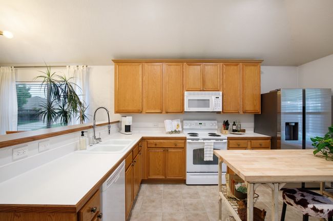 Kitchen featuring white appliances, light countertops, light tile patterned floors, and a peninsula | Image 9