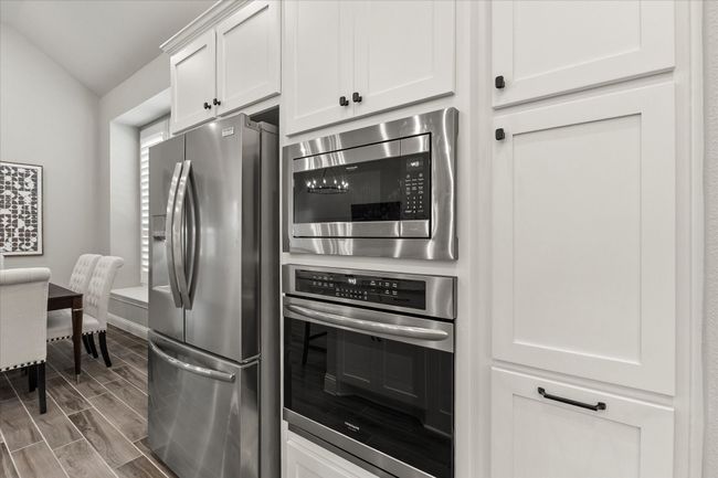 Kitchen with stainless steel appliances, wood tiled floors, white cabinetry, and vaulted ceiling | Image 17