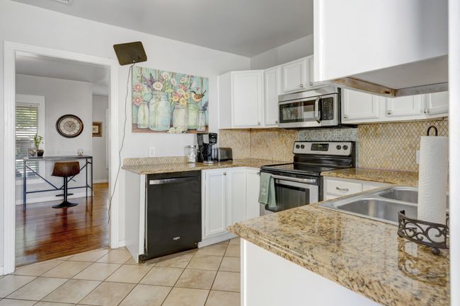 Kitchen featuring white cabinetry, sink, backsplash, light tile patterned floors, and appliances with stainless steel finishes | Image 9