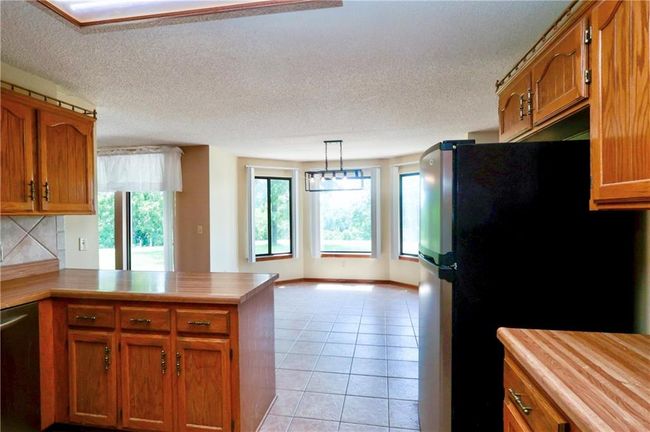 Kitchen with a peninsula, brown cabinetry, light countertops, stainless steel dishwasher, and a textured ceiling | Image 18