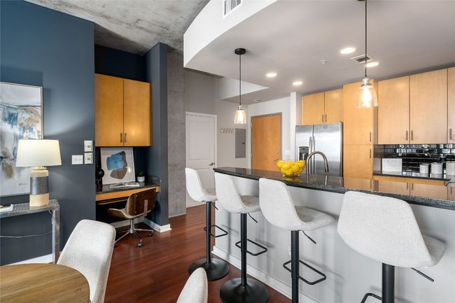 Kitchen featuring stainless steel fridge, dark wood-style flooring, dark stone countertops, a kitchen bar, and decorative light fixtures | Image 4