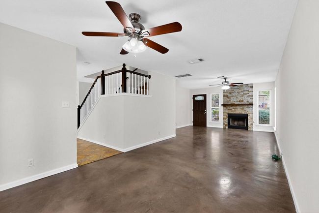 Unfurnished living room featuring ceiling fan, concrete floors, baseboards, and stairway | Image 9