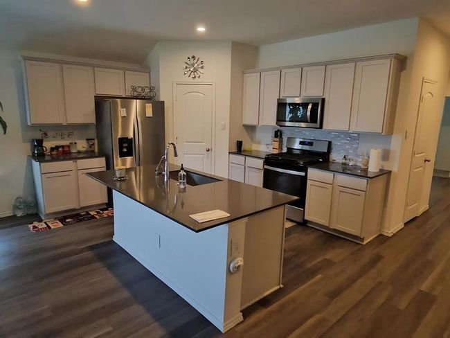 Gourmet kitchen featuring granite countertops, stainless steel appliances, ample cabinetry, and a large center island with bar seating. | Image 4