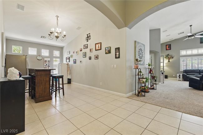 Dining area featuring arched walkways, light tile patterned flooring, baseboards, light colored carpet, and ceiling fan with notable chandelier | Image 5