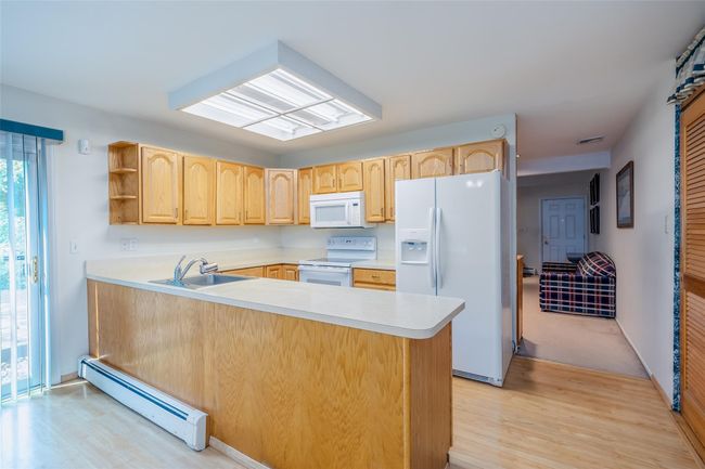 Kitchen with white appliances, a baseboard radiator, a sink, light brown cabinets, and light wood finished floors | Image 14