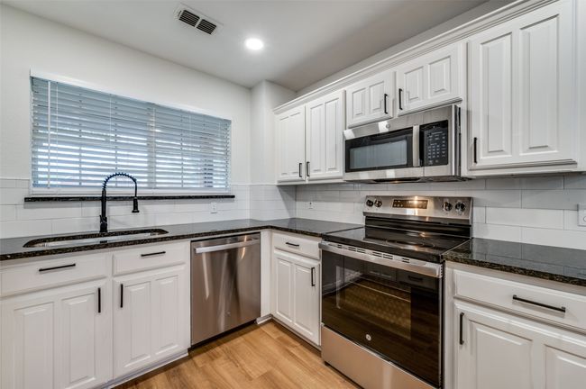 Kitchen featuring tasteful backsplash, white cabinetry, visible vents, a sink, and stainless steel appliances | Image 12