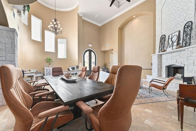 Dining area with crown molding, a fireplace, a high ceiling, stone tile flooring, and ceiling fan with notable chandelier | Image 8