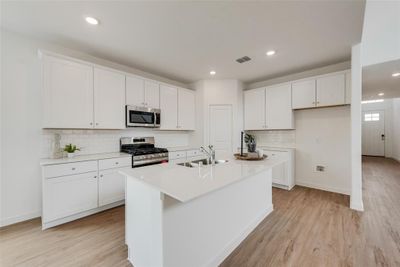 Kitchen featuring an island with sink, appliances with stainless steel finishes, white cabinetry, light wood-type flooring, and sink | Image 2