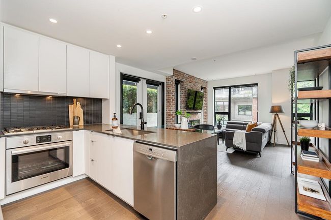 Kitchen featuring a peninsula, appliances with stainless steel finishes, decorative backsplash, light wood finished floors, and white cabinetry | Image 4