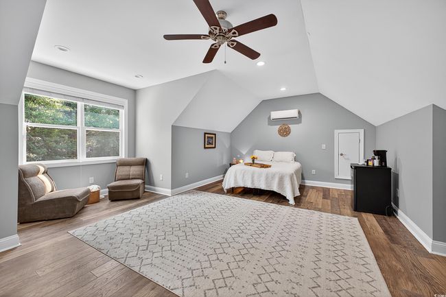 Bedroom with a wall unit AC, vaulted ceiling, wood finished floors, a ceiling fan, and recessed lighting | Image 34