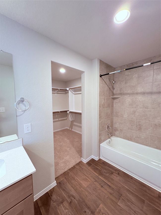 Bathroom with wood finished floors, vanity, a walk in closet, baseboards, and bathtub / shower combination | Image 36