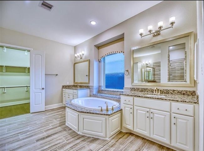This bathroom features a spacious layout with a large soaking tub, dual vanities with granite countertops, and elegant lighting. It includes a separate walk-in closet and a shower, all with modern finishes and neutral tones. | Image 29