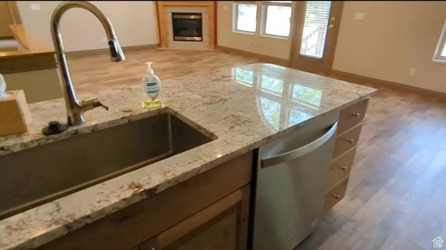 Kitchen with dishwasher, a sink, light stone countertops, light wood finished floors, and a glass covered fireplace | Image 12