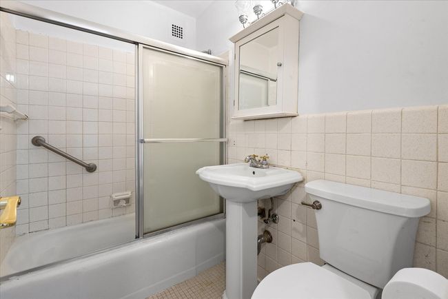Bathroom with enclosed tub / shower combo, toilet, tile patterned flooring, and tile walls | Image 14