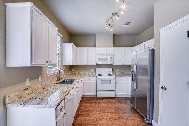 Kitchen with white appliances, a sink, white cabinets, and dark wood-type flooring | Image 7