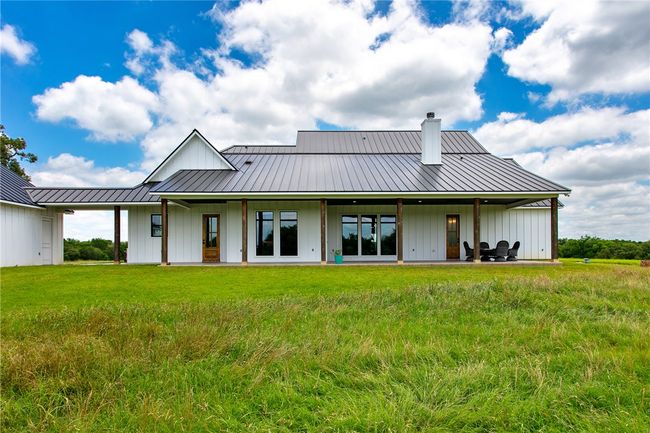 Rear view of house featuring board and batten siding, a chimney, metal roof, and a yard | Image 30