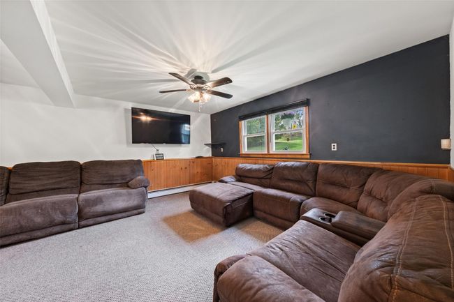 Living room featuring a baseboard radiator, wainscoting, carpet, a ceiling fan, and wooden walls | Image 22